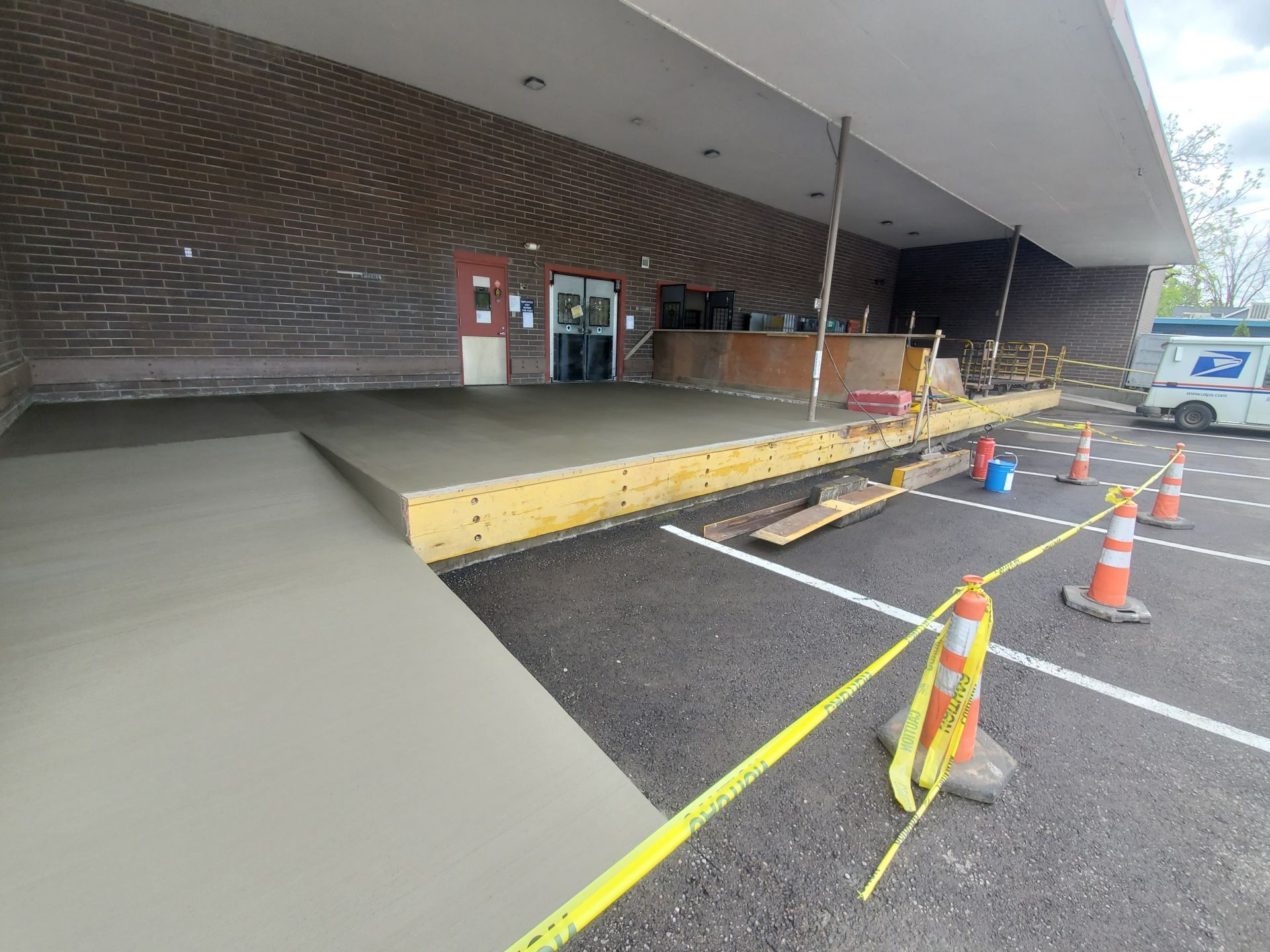 Newly poured concrete ramp and entrance under construction; safety cones and caution tape present.
