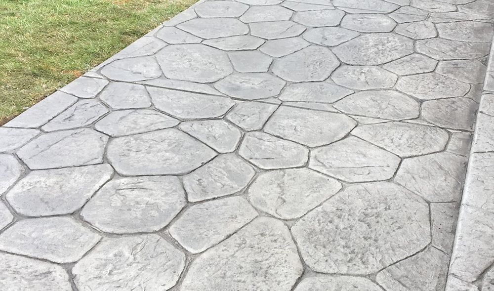 Gray concrete walkway with a cobblestone pattern next to green grass.