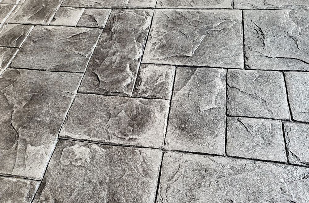 Gray, stone-textured concrete paving, showing rectangular and irregular shapes.