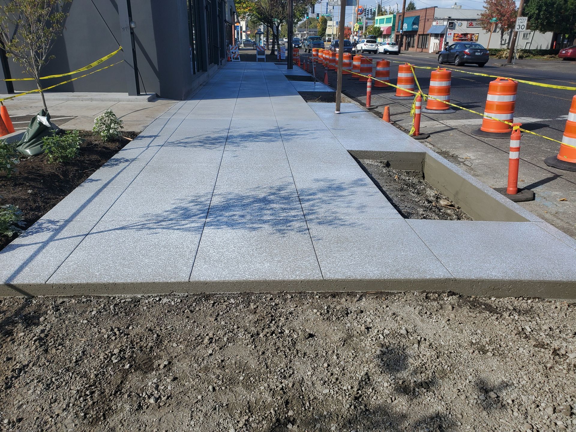 Sidewalk under construction with gray pavers, concrete border, and orange traffic cones.