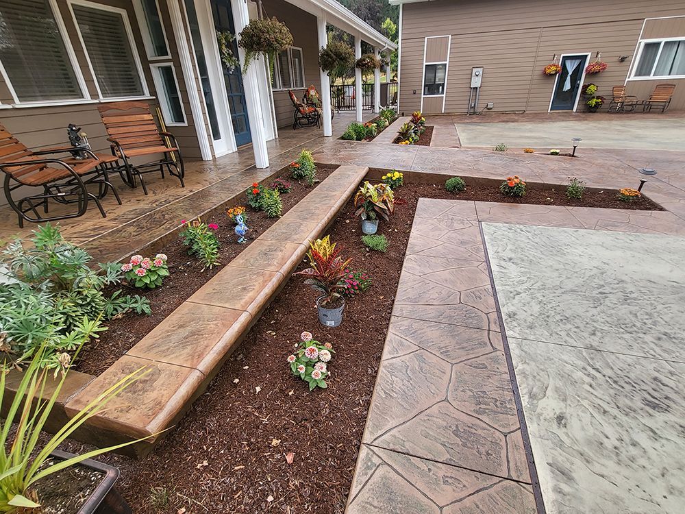 A courtyard with stamped concrete walkways and raised flower beds filled with colorful plants.