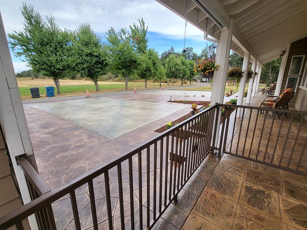 View from a porch with a brown railing, overlooking a concrete patio and trees under a cloudy sky.