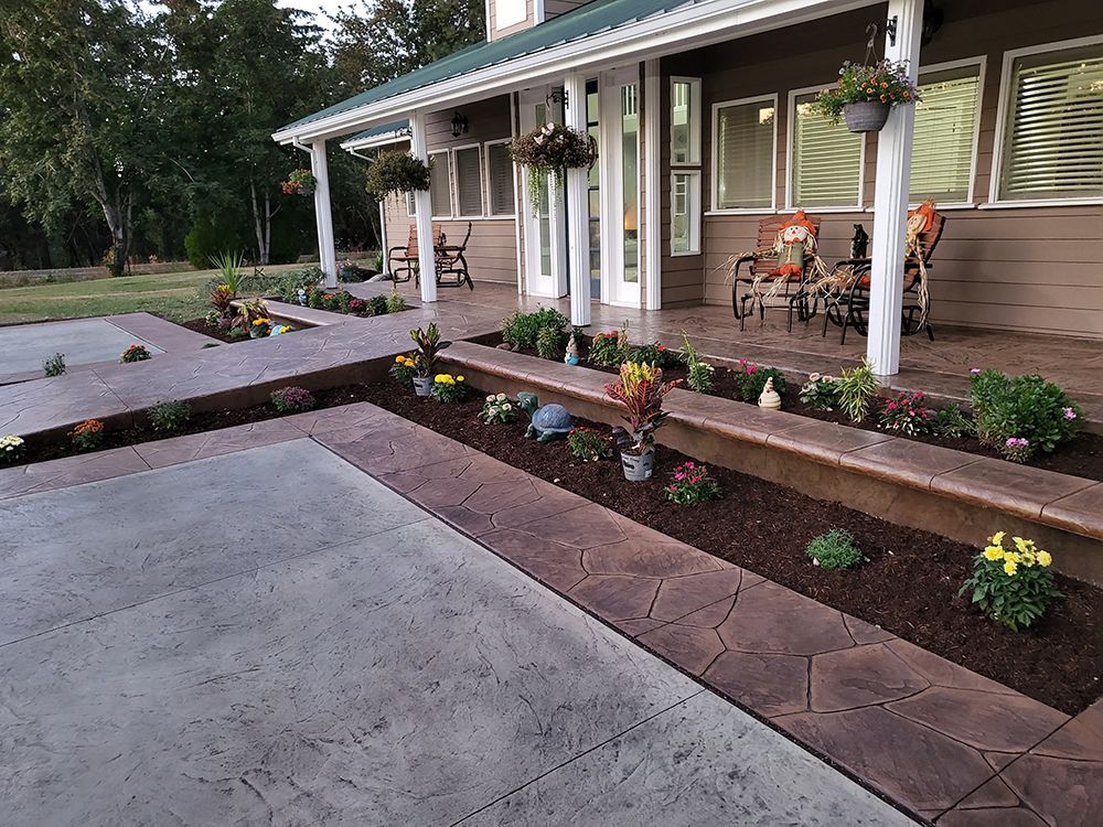 A house with a porch and flower beds. Concrete walkway with landscaping. Brown and yellow flowers.