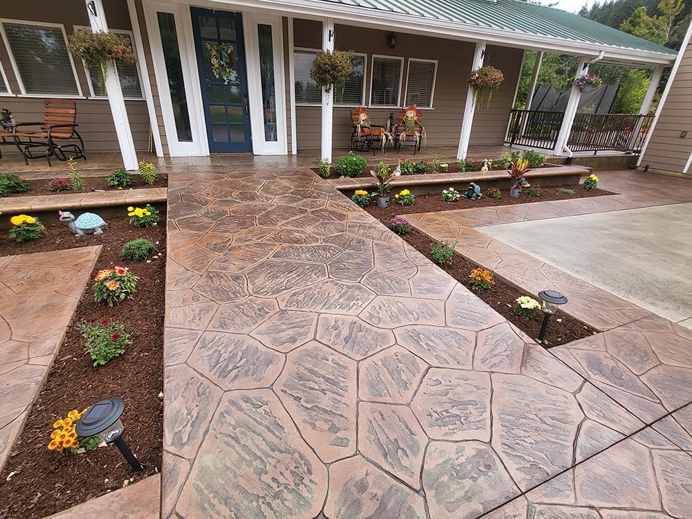 Stamped concrete walkway and flower beds leading to a house with a porch and blue door.