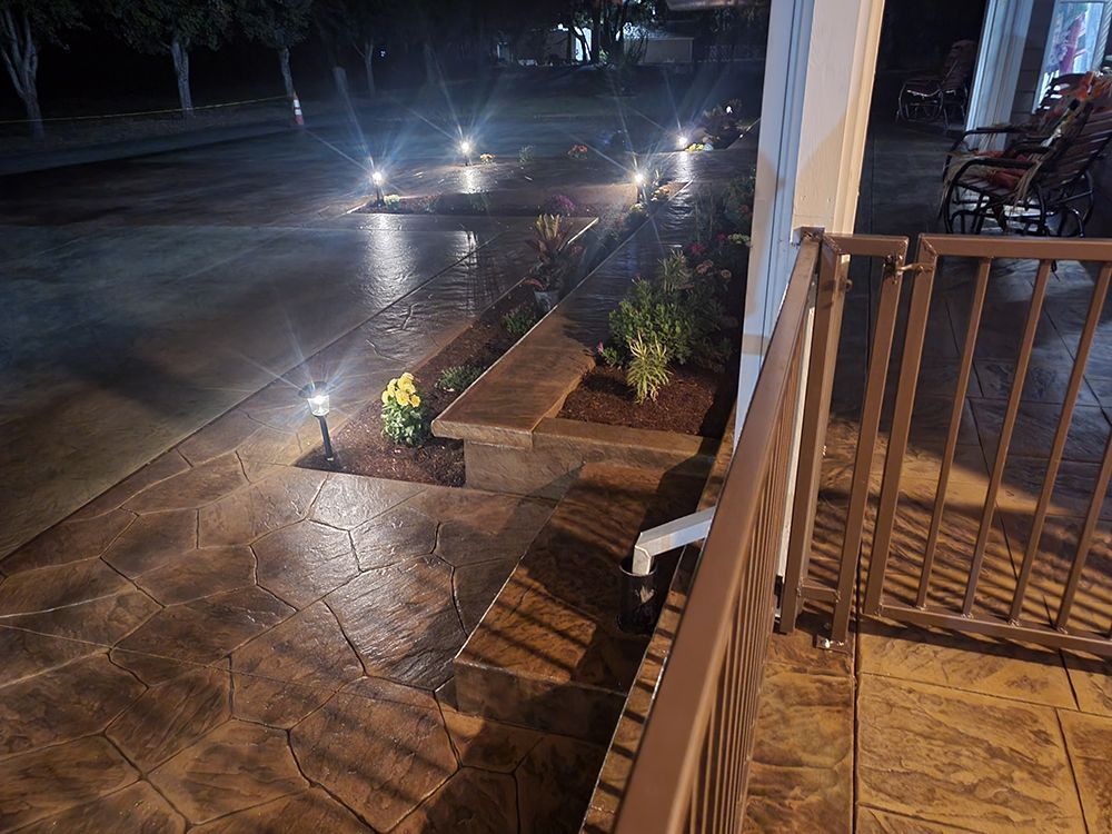 Pathway with stamped concrete, landscape lighting, and a porch with railing at night.
