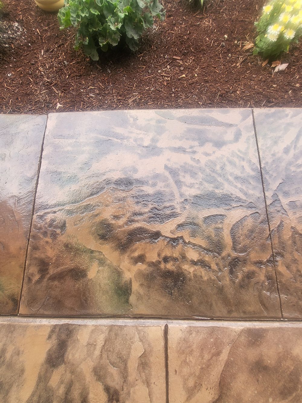 Stamped concrete walkway with brown and tan color variations, near a flower bed with mulch.