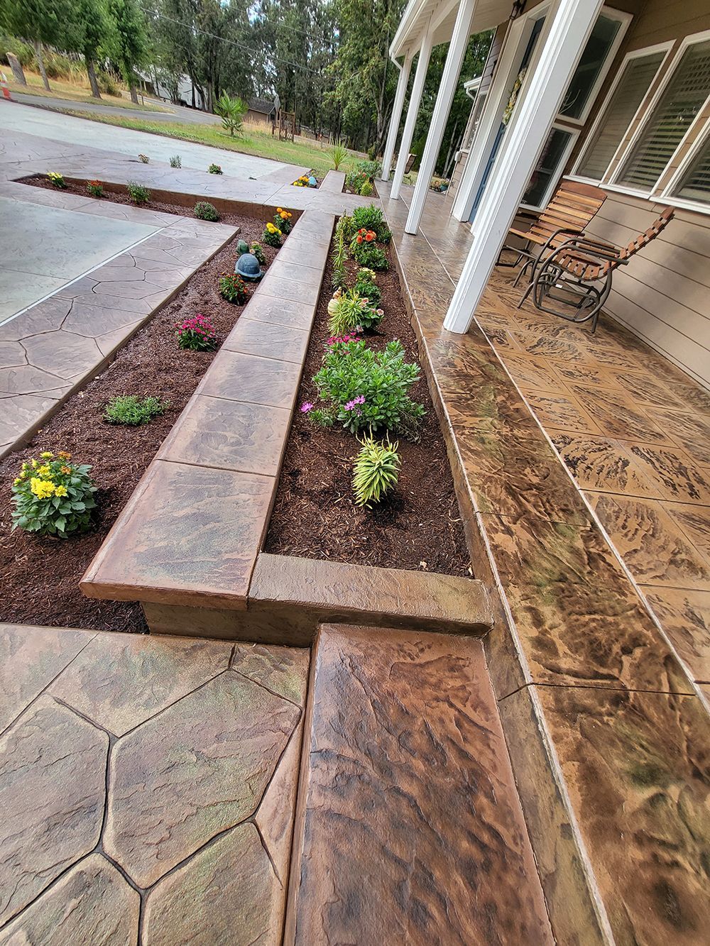 Stamped concrete walkway with flowerbeds along the house. Brown hues.