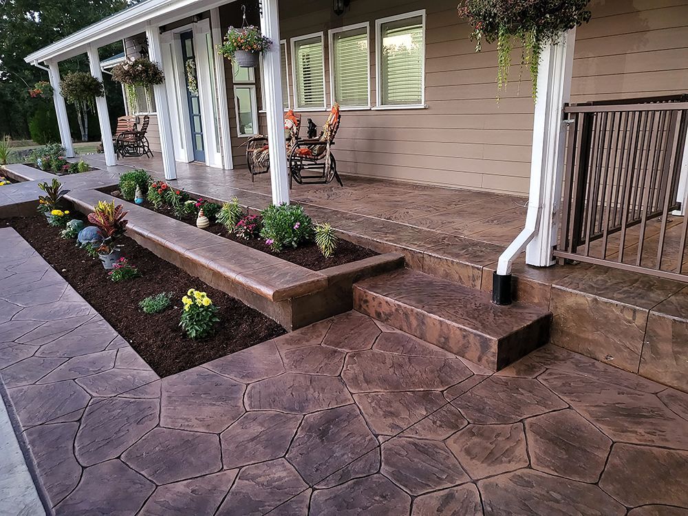 Brown stamped concrete patio and walkway with planter boxes and house.