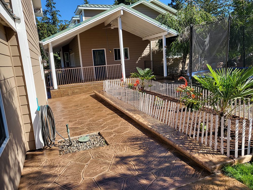 Brown stamped concrete patio with white picket fence, leading to a covered structure.