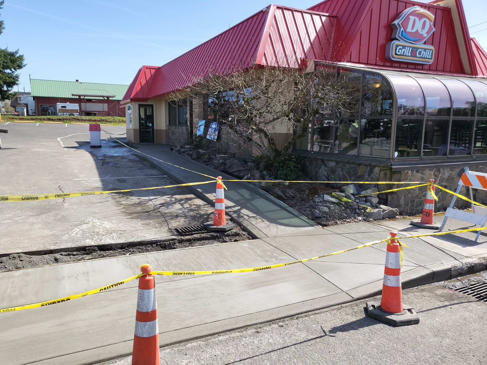 Sidewalk construction outside a Dairy Queen, with orange cones, caution tape, and a new concrete ramp.