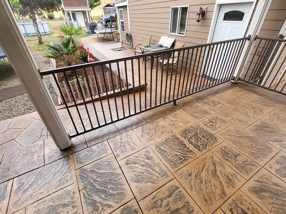 Brown stamped concrete patio with dark railing, planter, and back door.