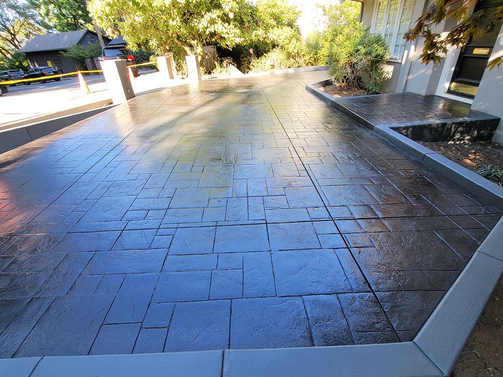 Dark gray stamped concrete driveway with a textured brick pattern.