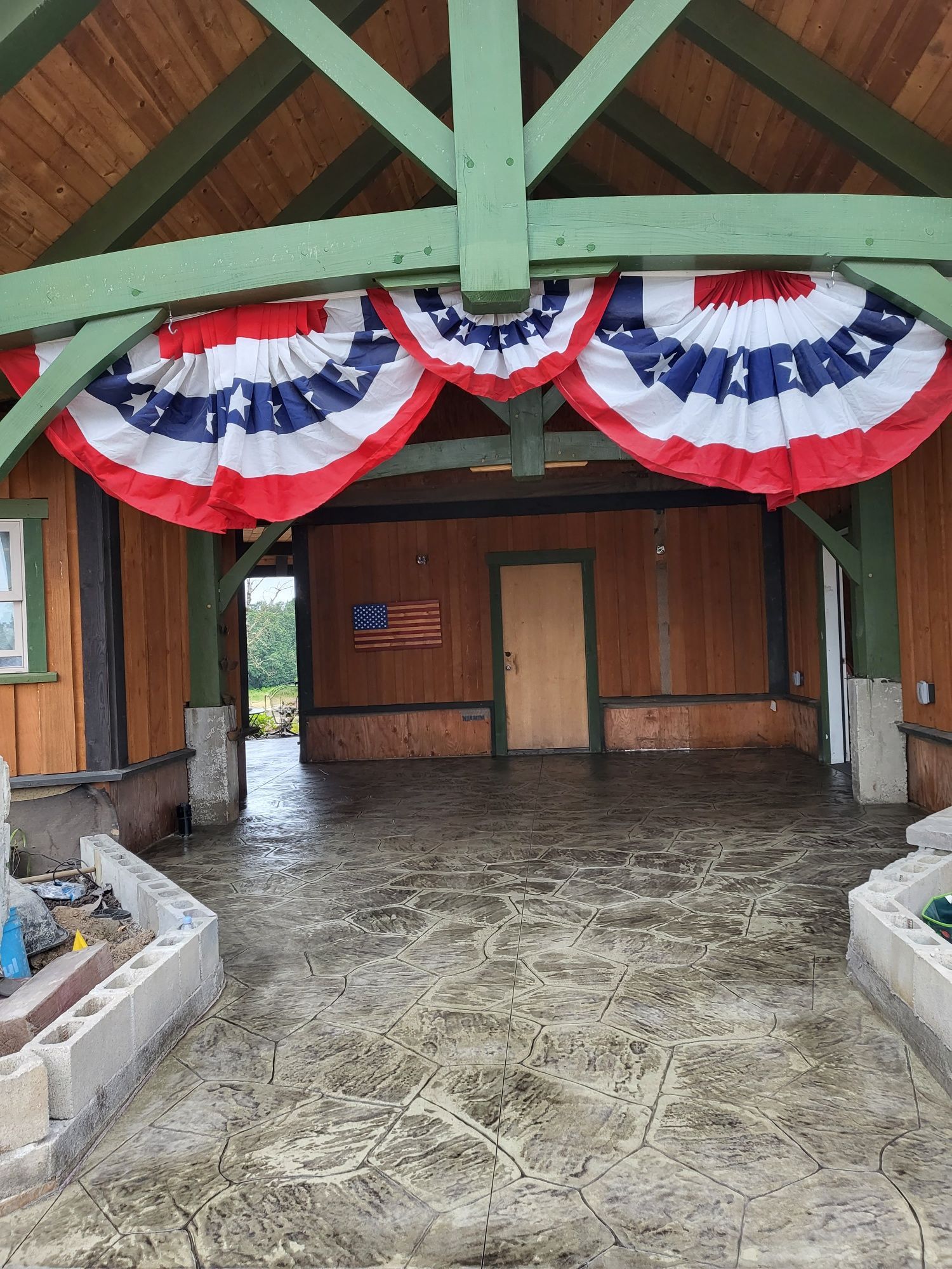 Covered porch with red, white, and blue bunting. Wooden walls, concrete floor, American flag artwork.
