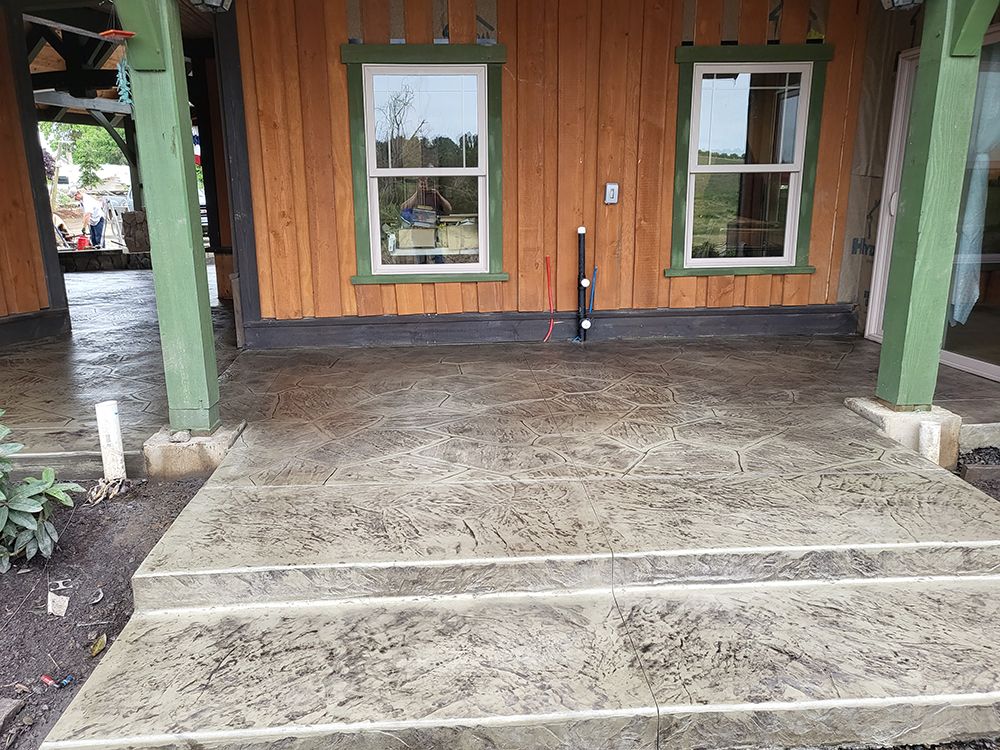 Concrete porch with steps, against a wood-paneled building with windows, green posts.