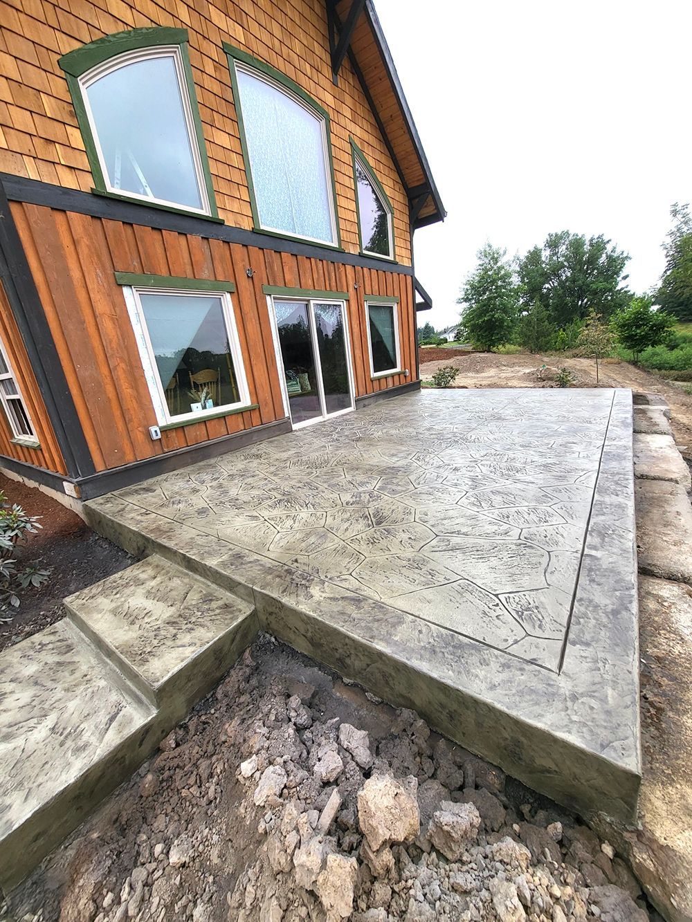 Concrete patio with steps adjacent to a wooden house with large windows.