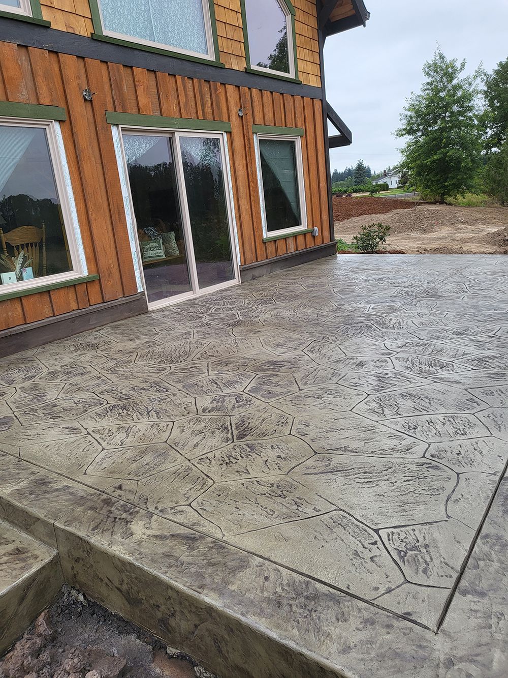 Concrete patio next to a house with sliding glass doors and windows; brown siding.