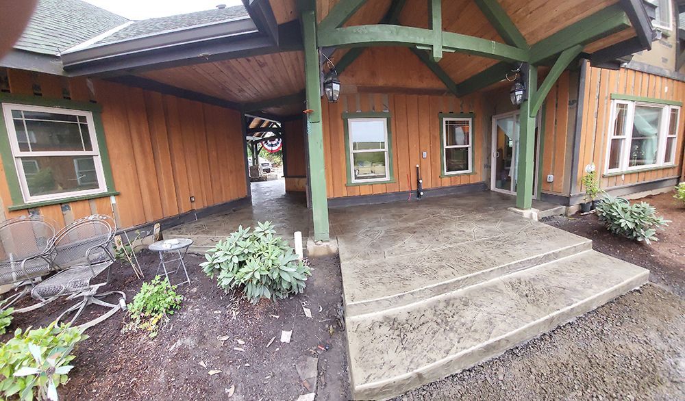 Exterior of a wooden house with a covered porch and concrete steps.