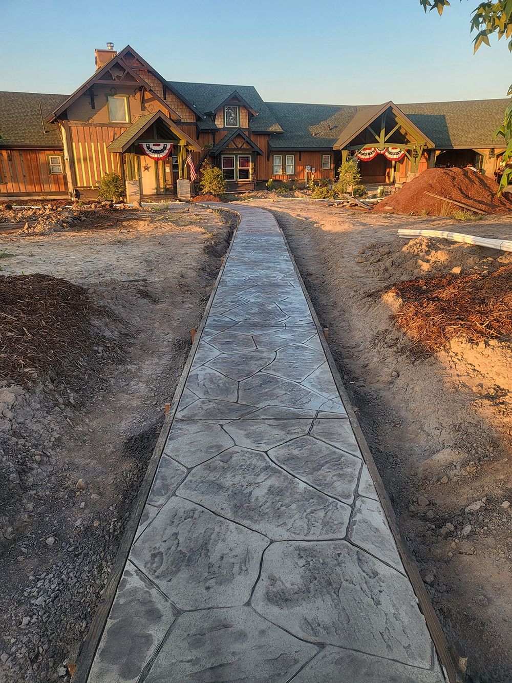 Concrete pathway leading to a large building, surrounded by dirt and landscaping materials.