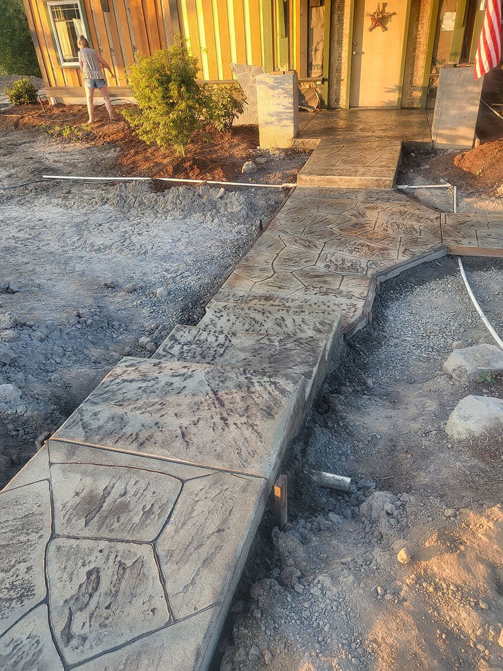 Concrete pathway leading to a house entrance; pathway has textured stone pattern, unfinished construction site.