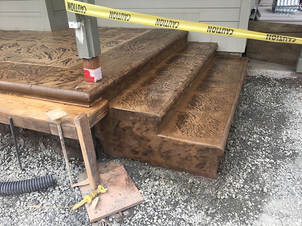 Brown concrete steps under a porch, blocked by caution tape. A wooden workbench and drain are in the foreground.
