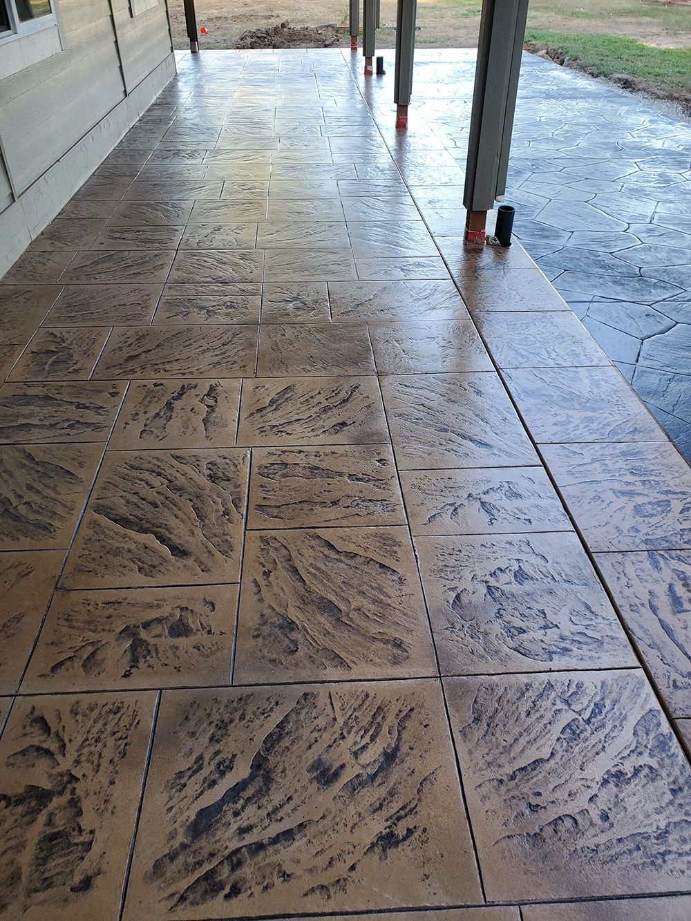 Brown and black textured concrete patio with a wet, shiny appearance, viewed from an angle.