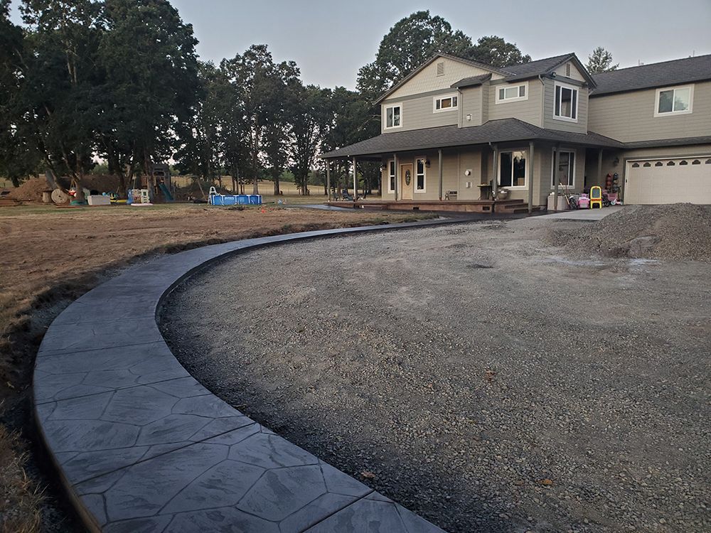 Curving concrete walkway leading to a two-story house with a porch and gravel driveway.