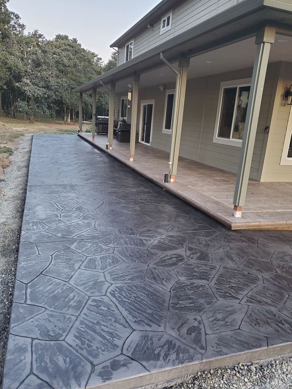 Concrete walkway with textured pattern next to a house with a porch.