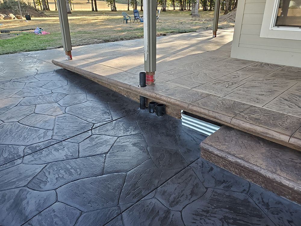 Stamped concrete patio with a step-down, surrounded by a house and pillars, featuring a stone pattern.