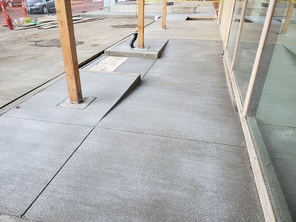 Concrete walkway with wooden pillars, a ramp, and building with glass windows.