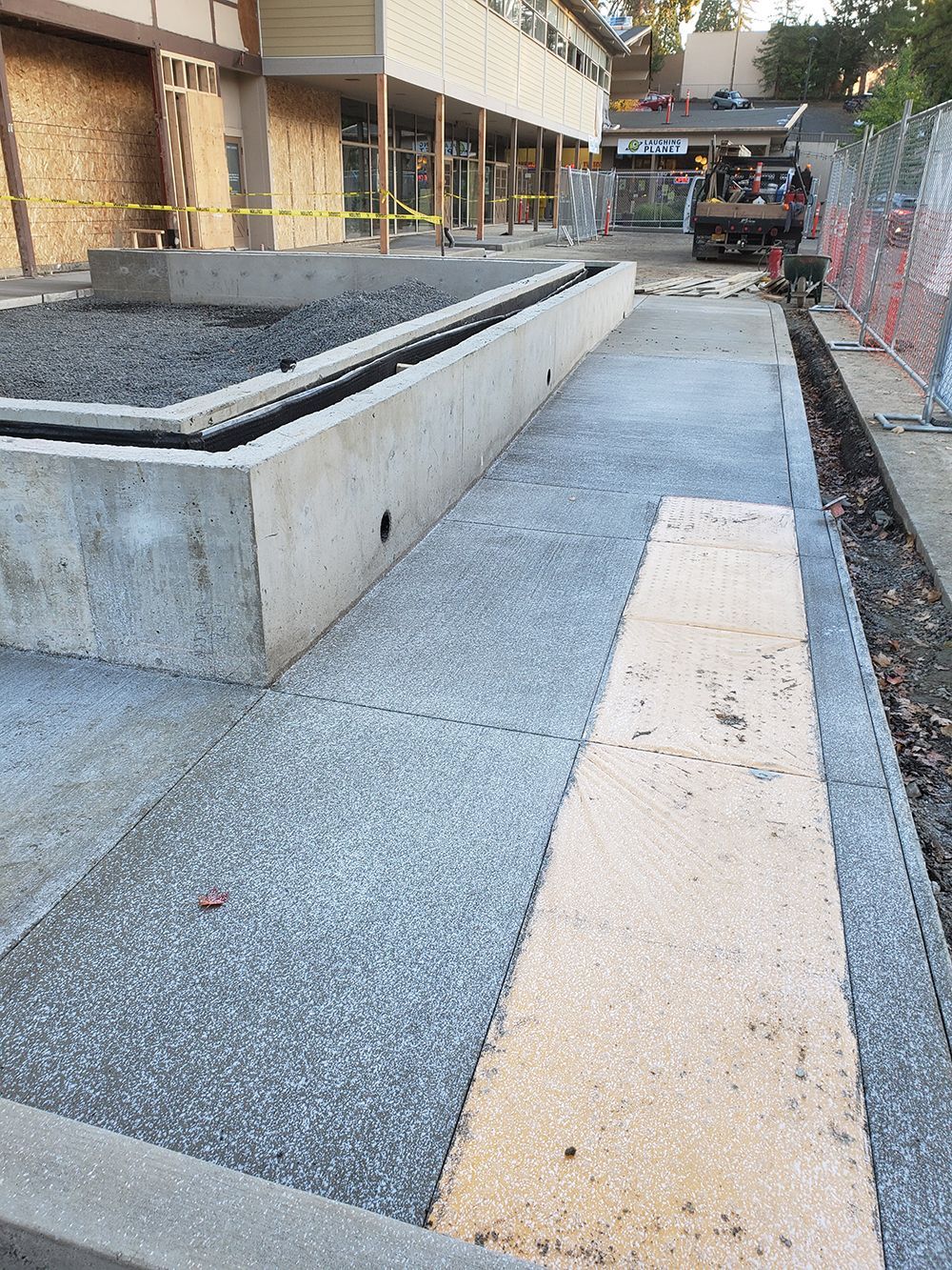 Concrete sidewalk with raised planters under construction near a building.