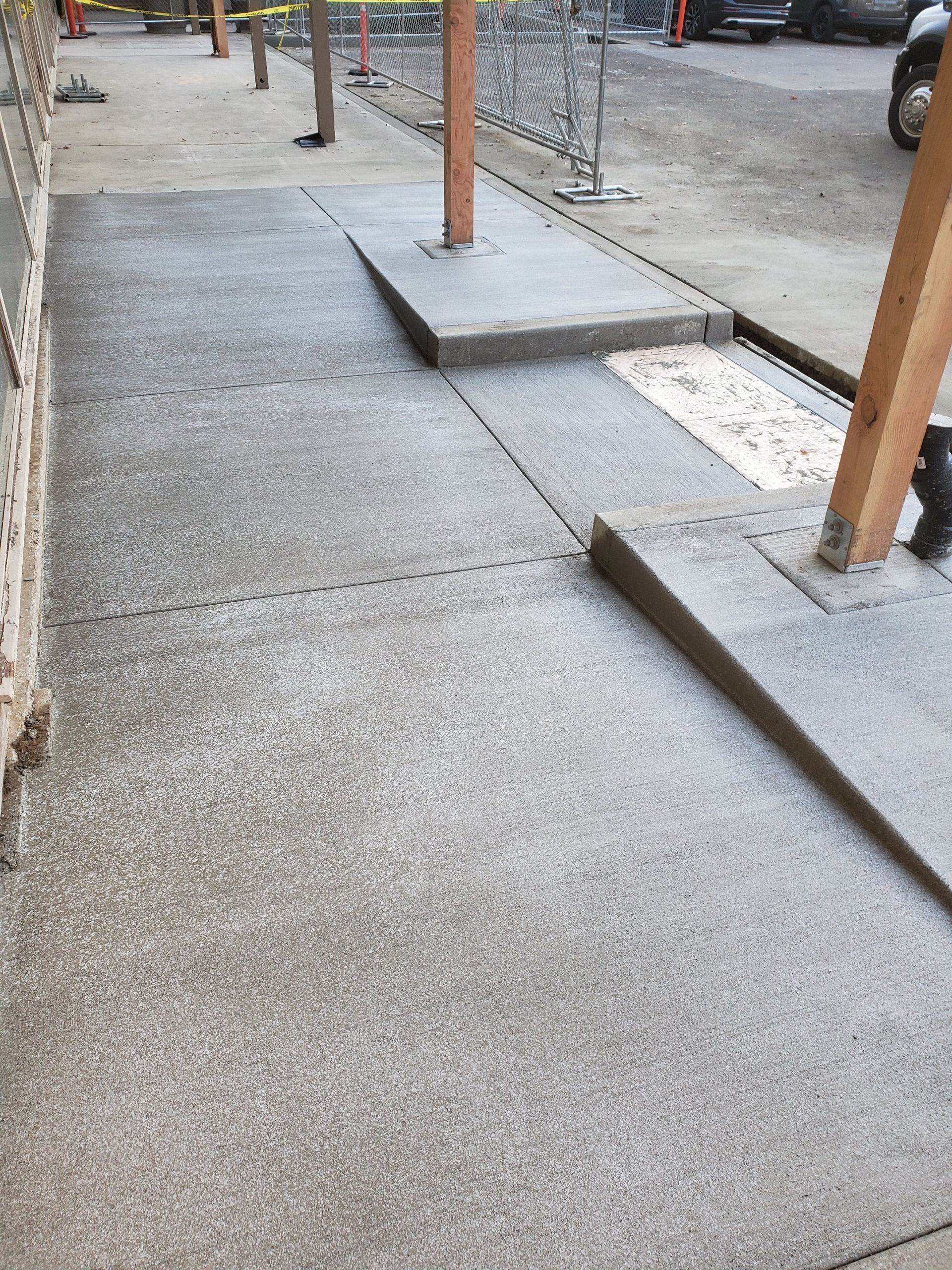 Sidewalk with two ramps for accessibility around wooden support beams.