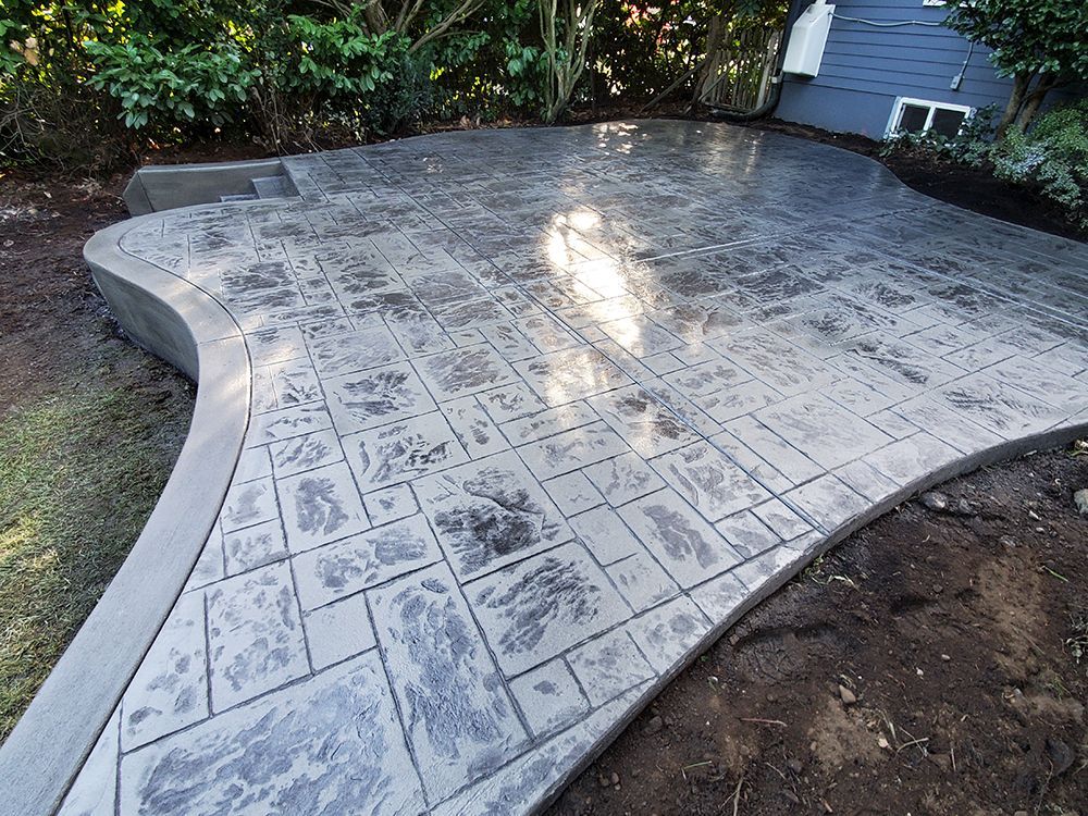 Gray, stamped concrete patio with curved edges and a house in the background.