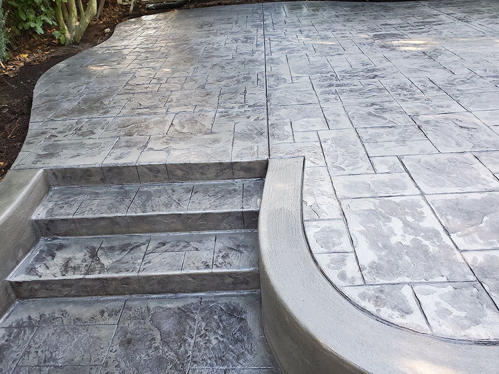 Gray concrete patio and steps with textured stone pattern.