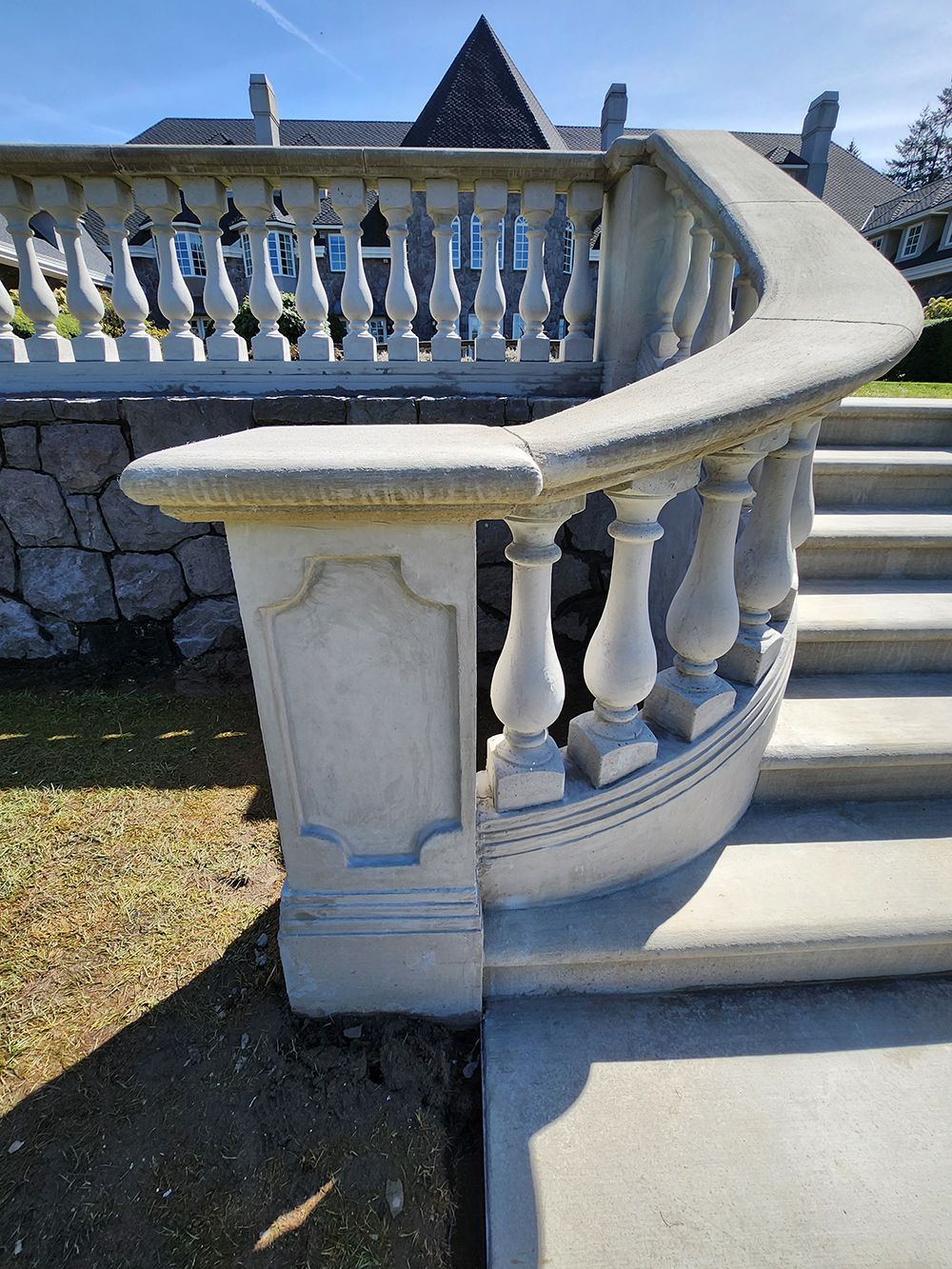 Concrete stairs with curved balustrade, leading up with stone wall background.