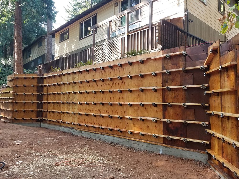 Wooden formwork for a retaining wall in front of a house, supported by metal hardware.