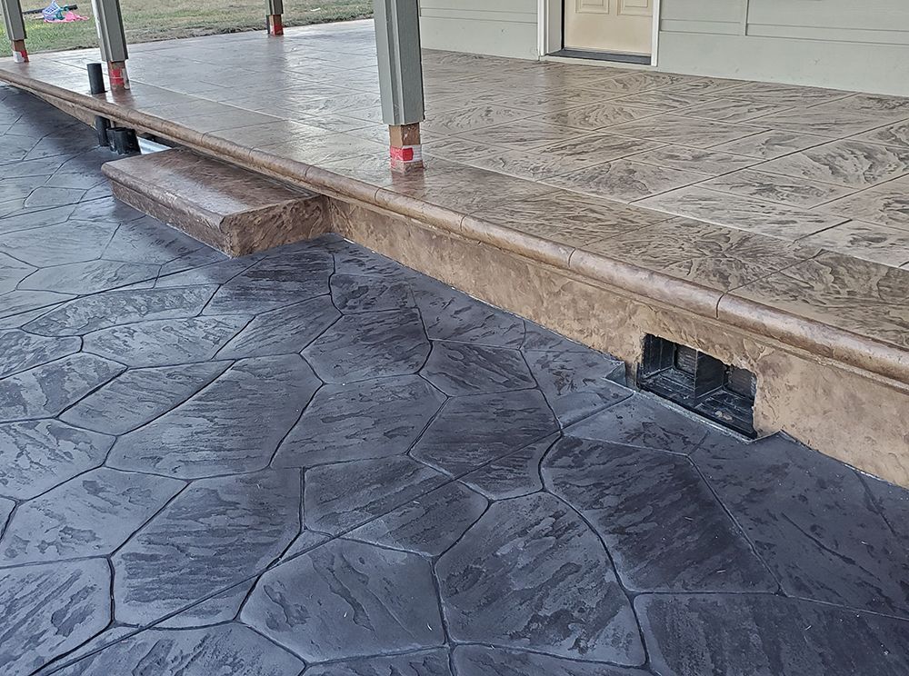 Stamped concrete patio with a dark grey stone pattern. It has a brown border and step.