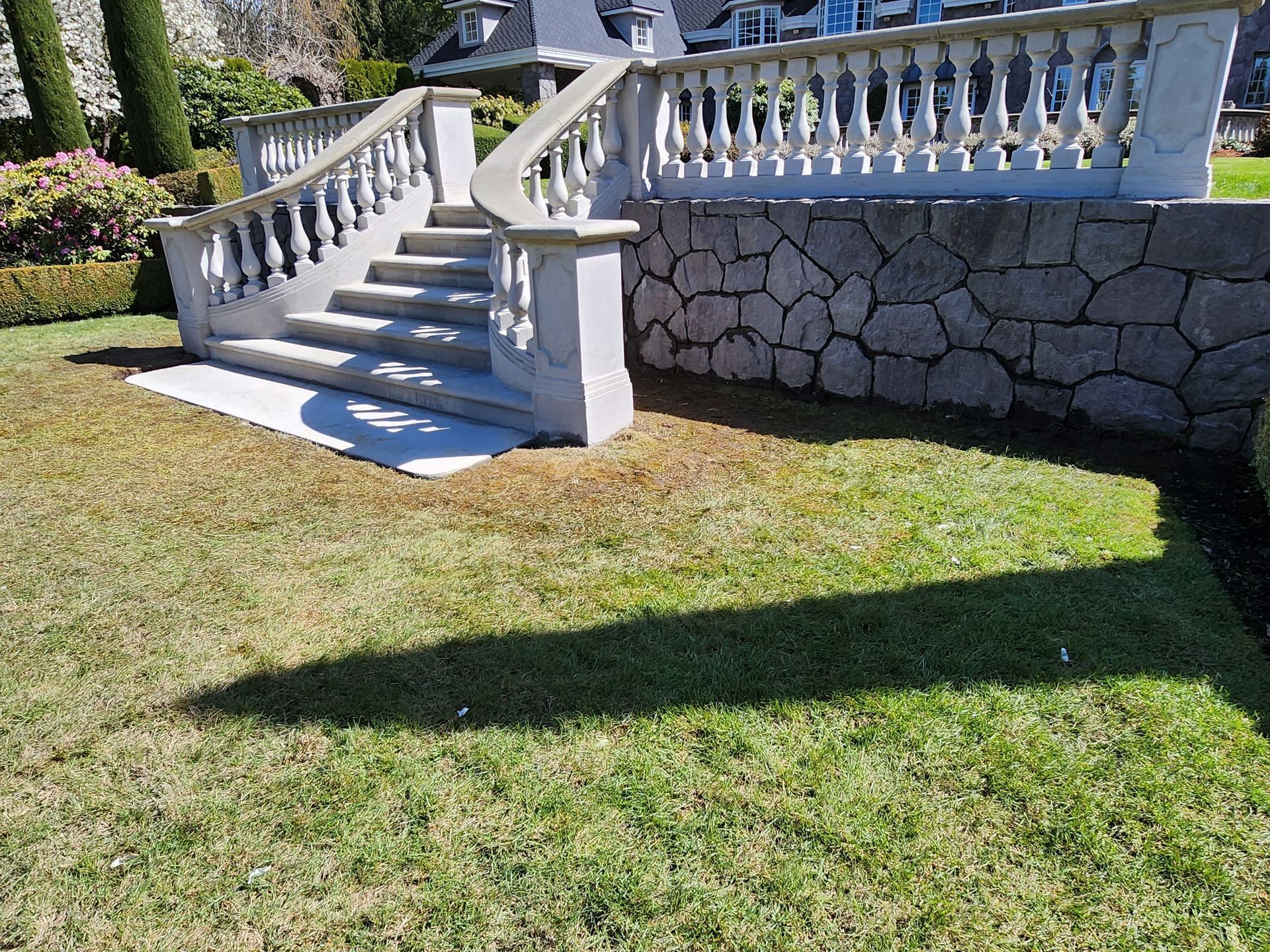 Stone staircase and wall in a grassy yard, cast shadow, topped with a balustrade.