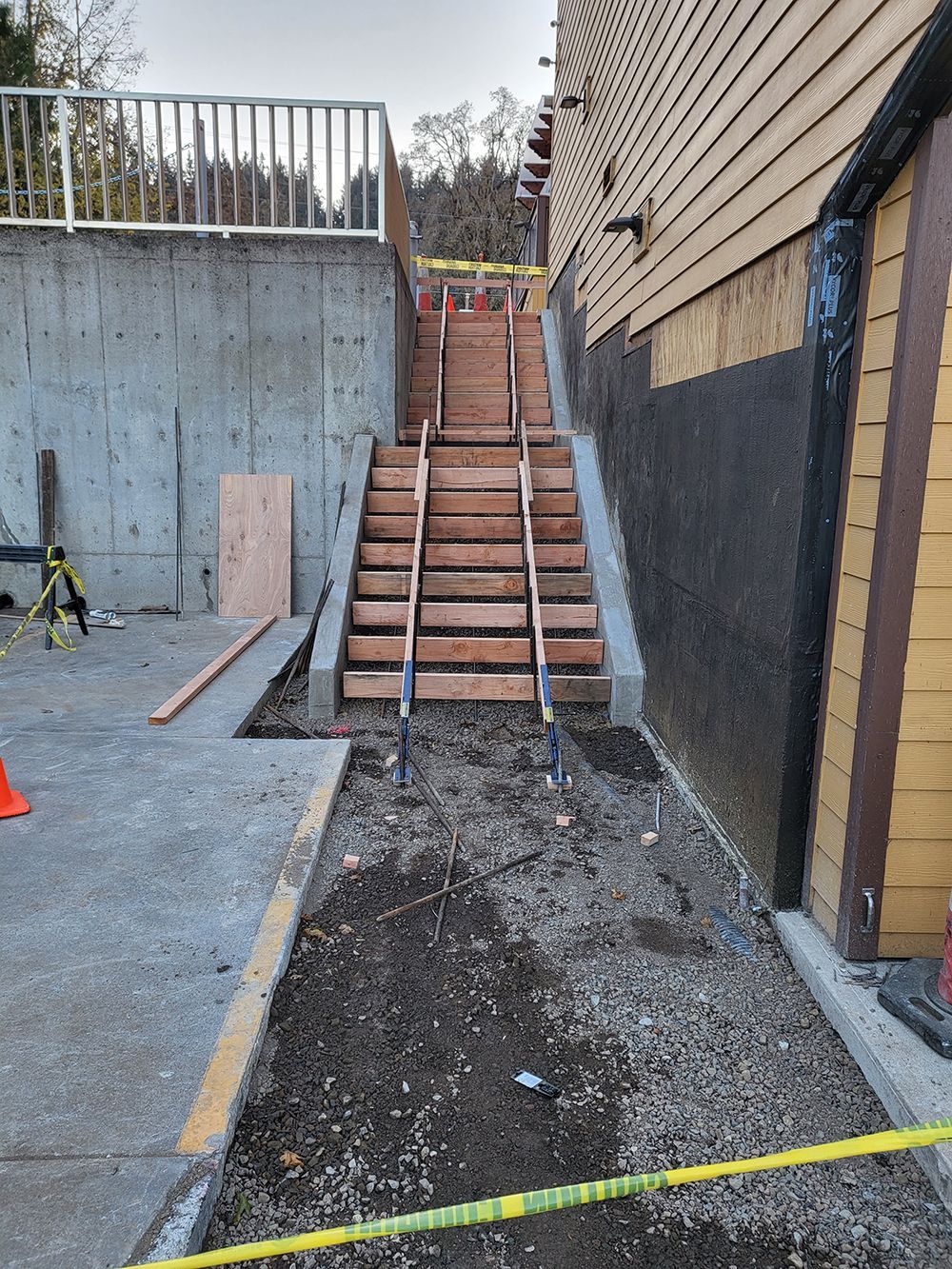 Staircase under construction; wooden forms on concrete steps, next to a building. Yellow caution tape and construction materials present.