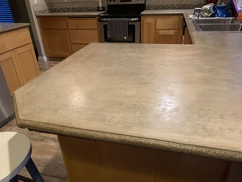 Kitchen with light wood cabinets, gray concrete countertop, stainless steel appliances.