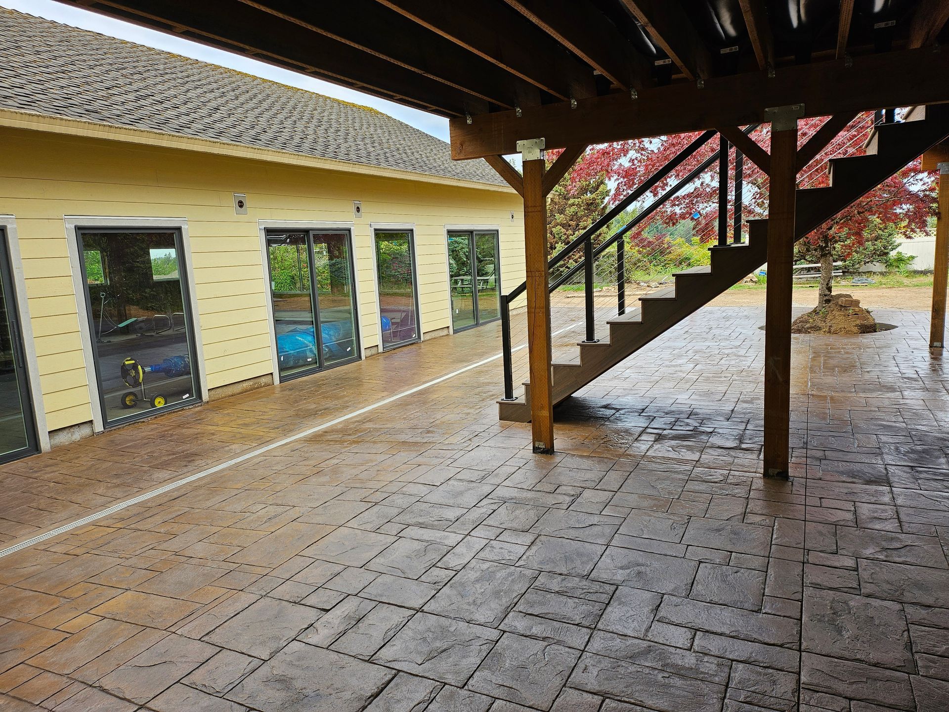 Patio with stone texture under wooden deck, stairs, glass doors, and yellow building.