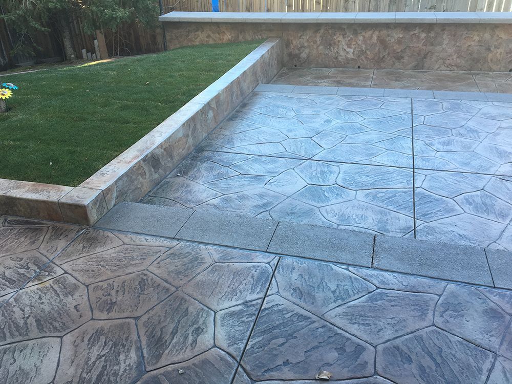 Patio with patterned gray concrete and a retaining wall bordering artificial turf.