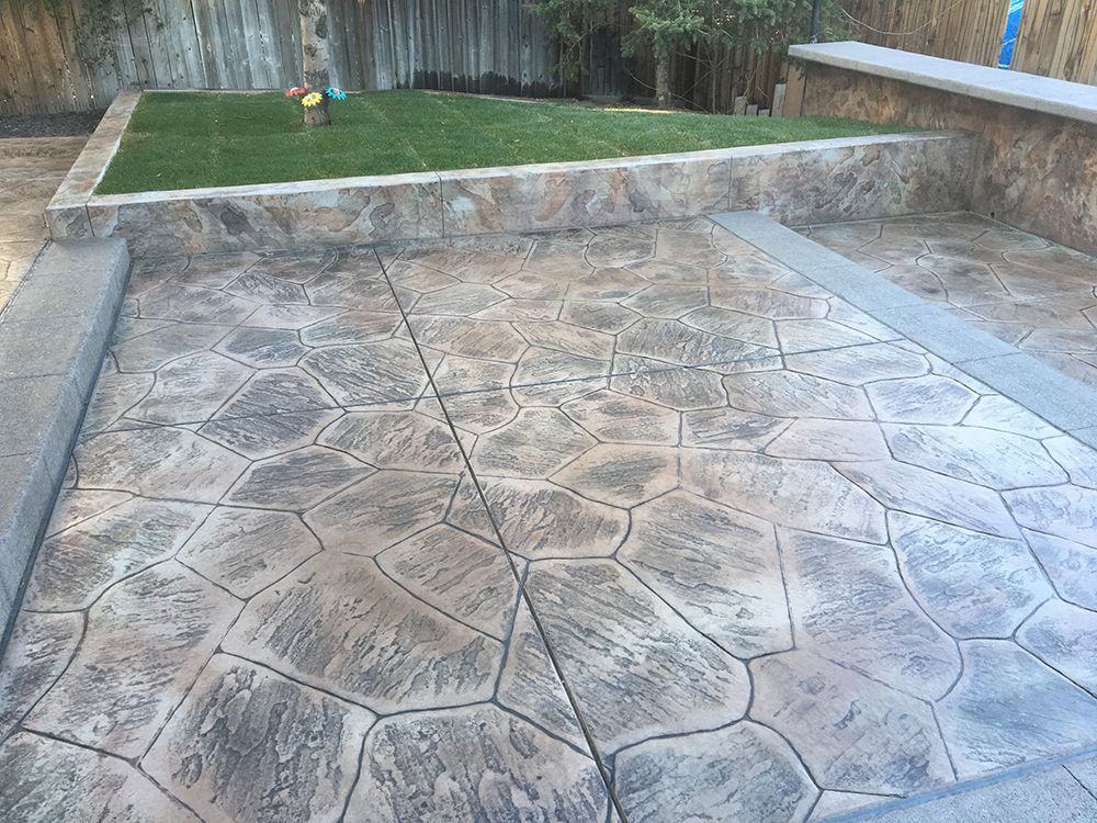 Stamped concrete patio with a raised lawn area and retaining wall.