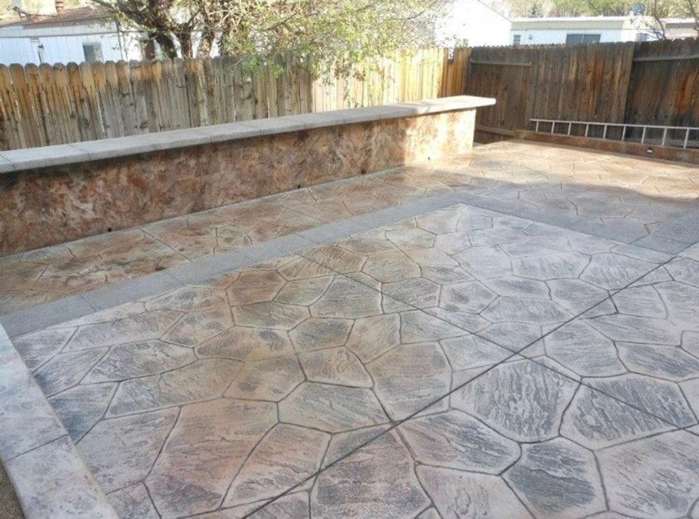 Stone-patterned concrete patio and low wall with wooden fence backdrop. Grey, brown, and tan tones in an outdoor setting.