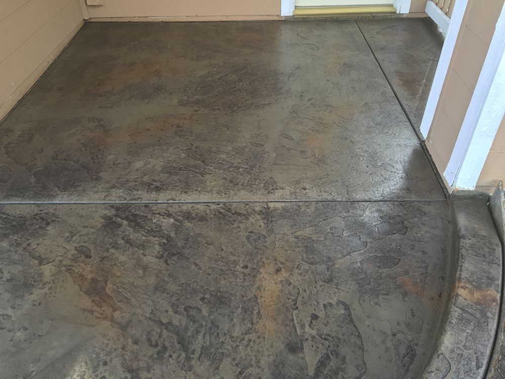 Concrete patio with mottled gray and brown coloring, next to a building with beige walls and a white column.