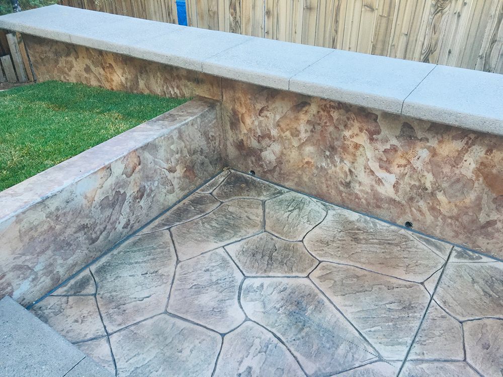 Stamped concrete patio with stone-patterned walls and grass. The color scheme is brown, tan and green.