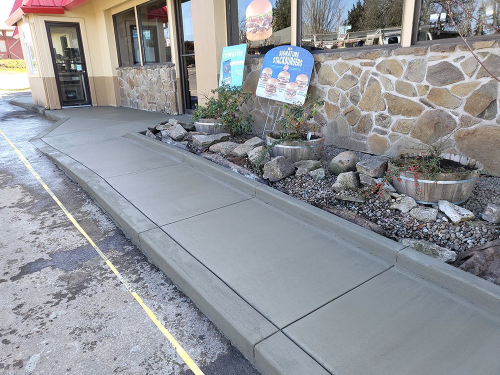 Newly poured concrete sidewalk with a ramp and bordering curb near a building.