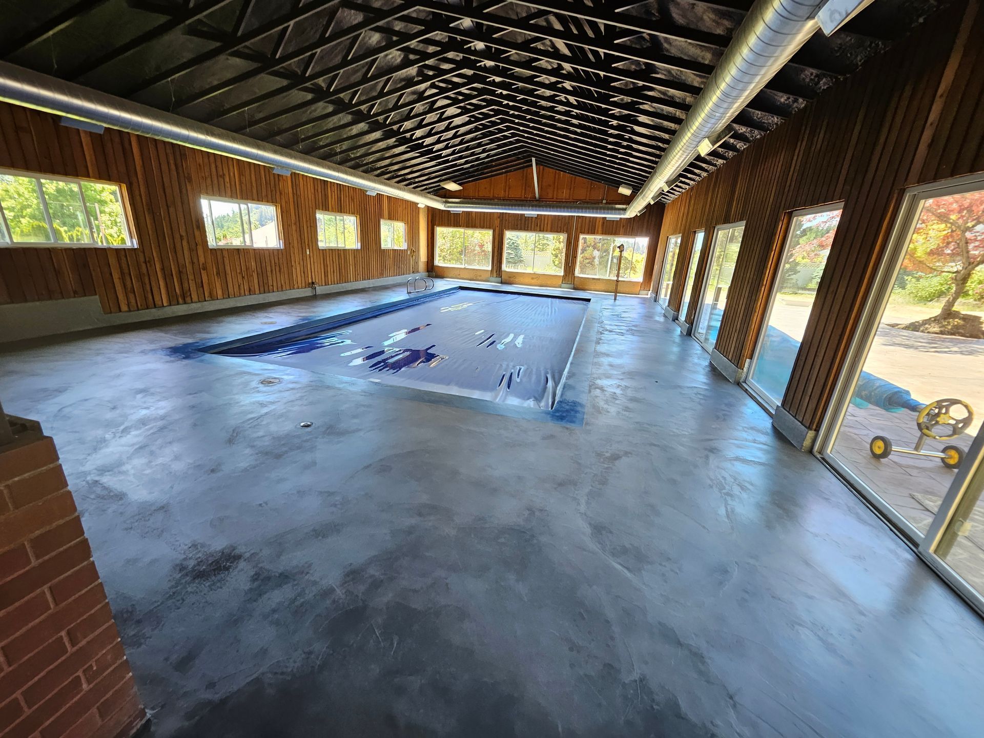 Indoor pool with a protective cover, surrounded by large windows, wood paneling, and a brick accent.