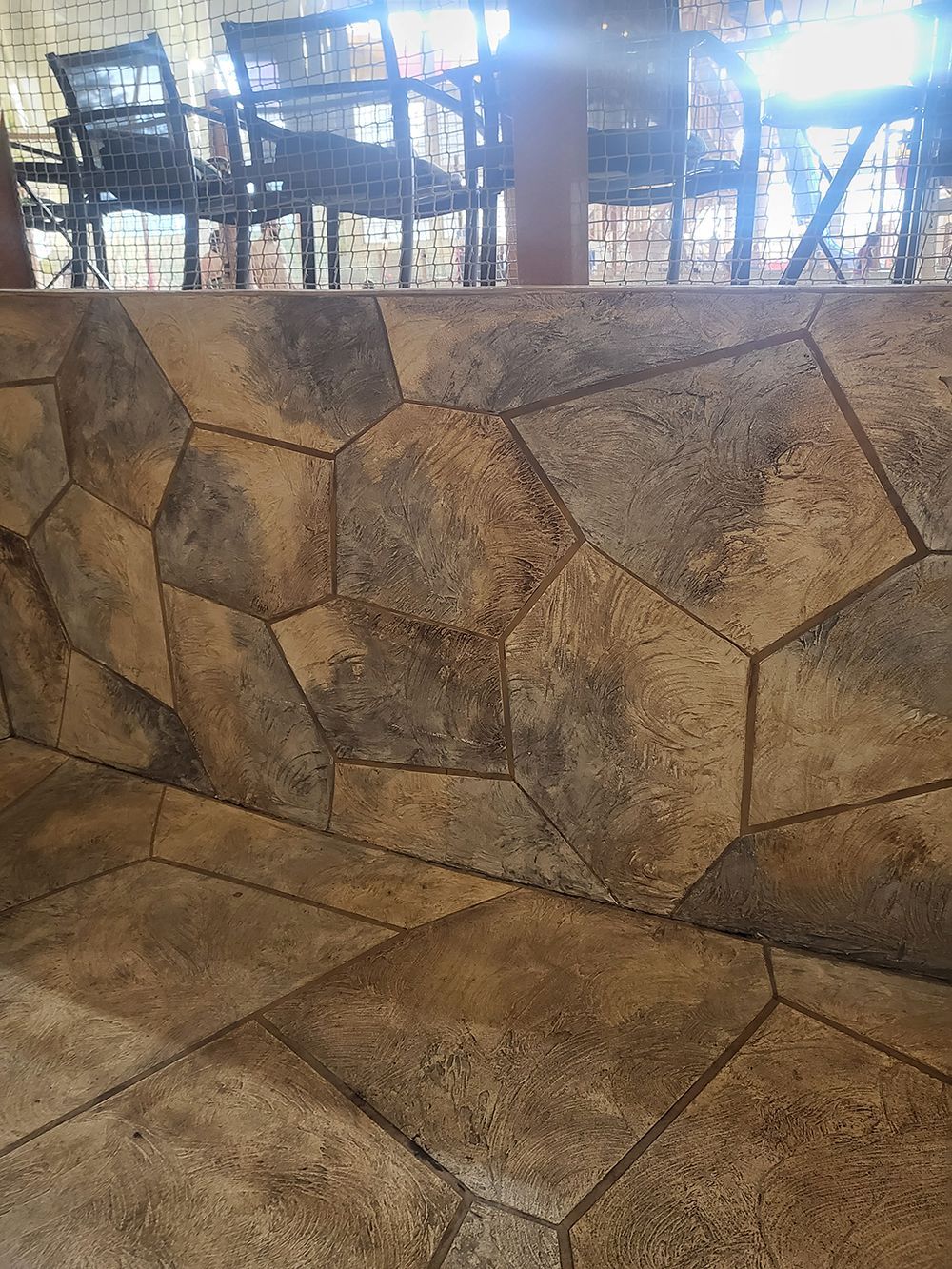 Stone wall and floor with tables and chairs visible in background.