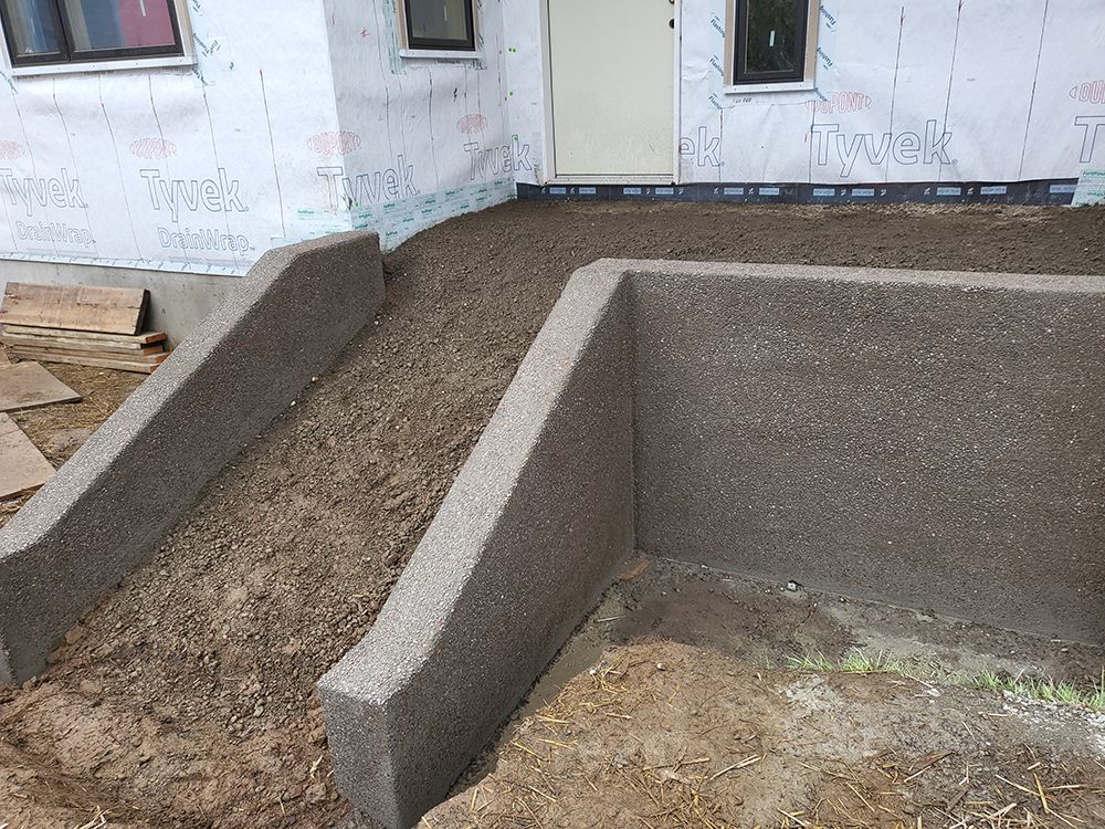 Concrete ramp leading to a doorway, with retaining walls made of similar material and surrounding dirt ground.