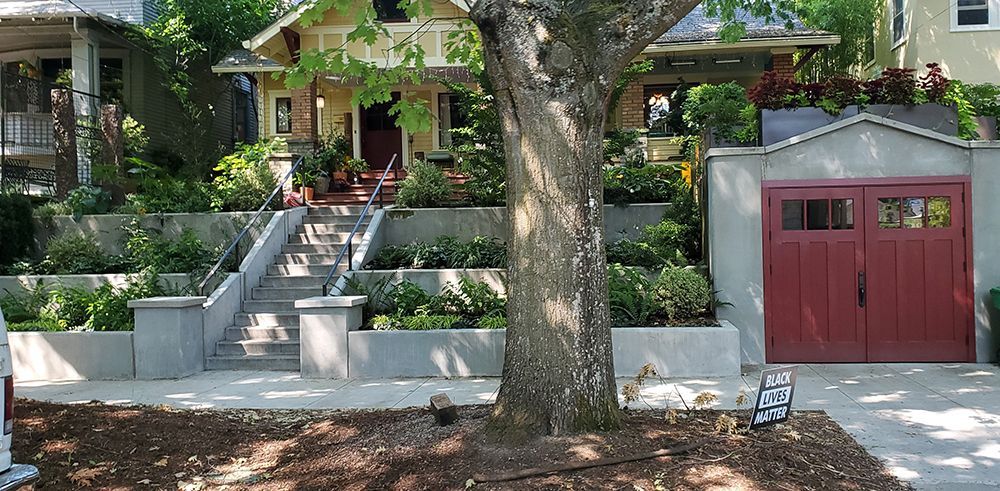 A yellow Craftsman home with a red garage; a large tree in the foreground.